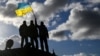 U.K. – Ukrainian personnel hold a Ukrainian flag as they stand on a Challenger 2 tank during training at Bovington Camp, near Wool in southwestern Britain, February 22, 2023